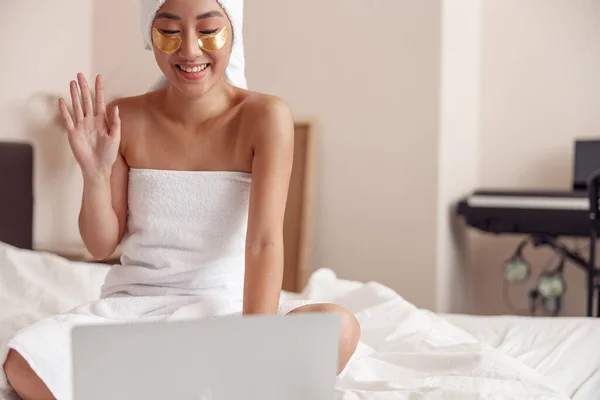 Joyful lady with gold patches under eyes doing hello gesture and smiling while talking with friend through video call