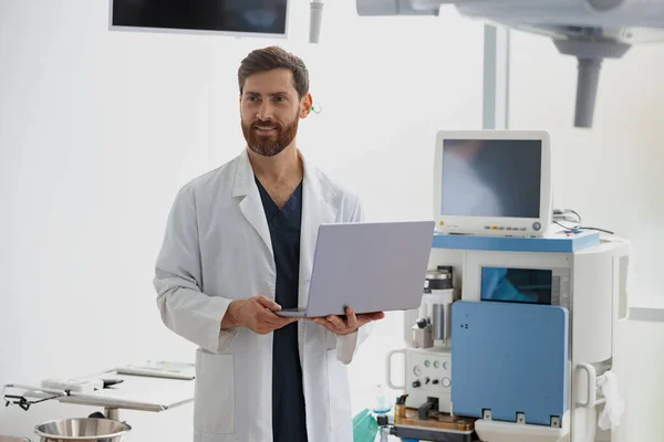 Professional doctor standing with laptop in operation room of modern clinic. High quality photo