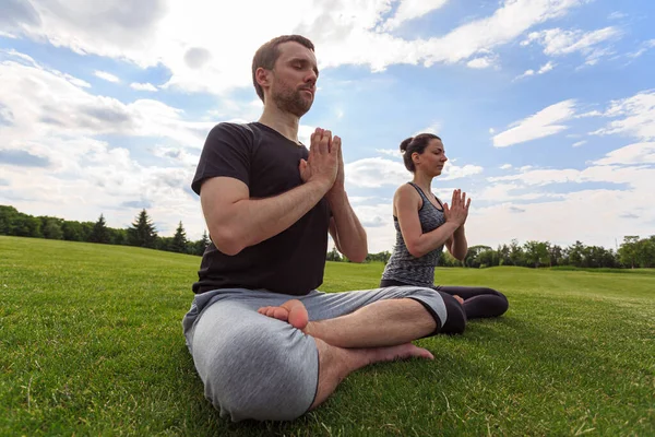 Young couple meditating in lotus position while doing yoga in park. High quality photo