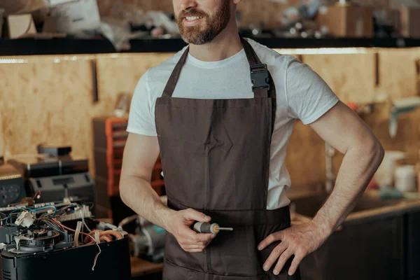 Unrecognizable smiling repairman with a screwdriver standing on own workshop with coffee machines