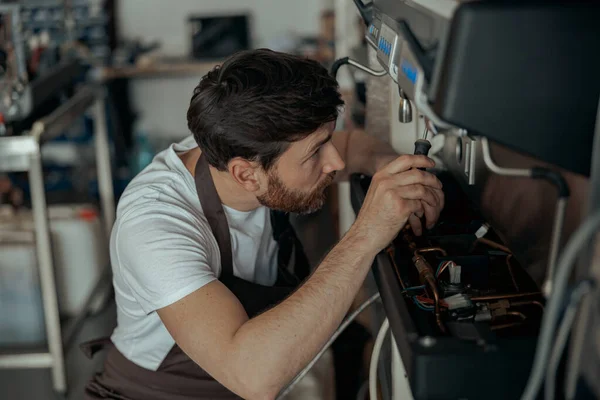 Repairman in uniform inspecting coffee machine in own workshop. High quality photo