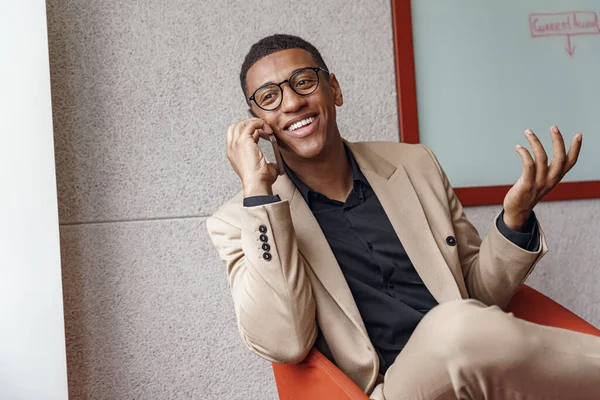 Smiling african businessman talking phone sitting in cozy coworking. High quality photo