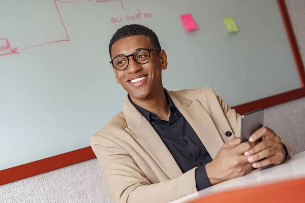 Handsome african businessman holding phone sitting in cozy coworking. High quality photo