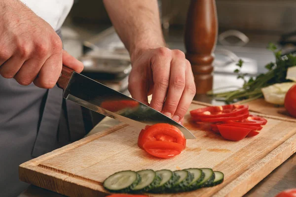Busy chef cutting tomatoes and cucumbers on a board in modern restaurant kitchen. High quality photo