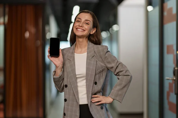 Portrait of attractive business woman with phone standing in modern coworking and looking camera