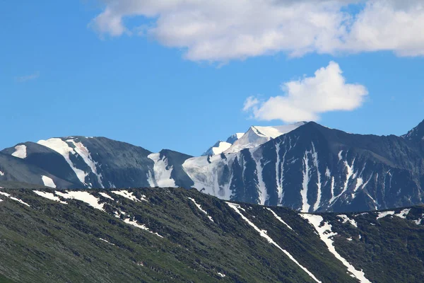 Snow-capped rocky ridges with peaks and glaciers against the sky with clouds in sunny summer weather