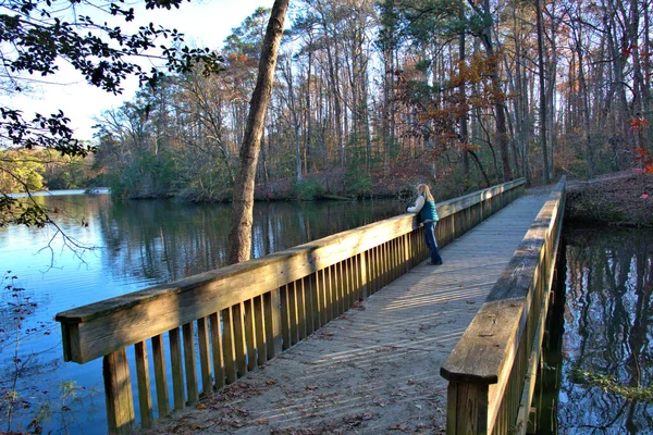 小さな湖を渡る橋の上で秋の色を楽しむ女性 — ストック写真