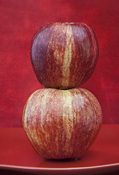 Dos manzanas apiladas una sobre la otra sobre fondo rojo texturizado —  Fotos de Stock