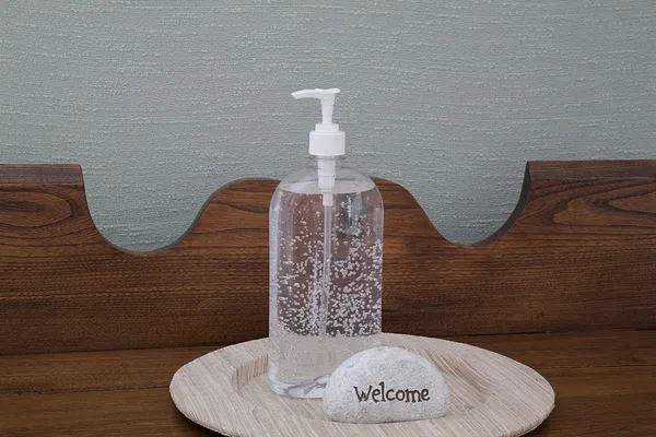 Desinfectante de mano transparente en una placa de lino única con señal de bienvenida Imagen de archivo