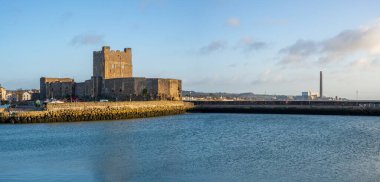 Kuzey İrlanda, Belfast yakınlarındaki Carrickfergus 'ta bulunan Ortaçağ Norman Kalesi' nin panoramasında kışın marina ve dalgakıran bulunur. Arka planda eski elektrik santrali
