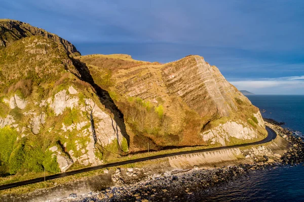 Northern Ireland, UK. Atlantic coast. Cliffs and Antrim Coast Road, a.k.a. Causeway Costal Route. One of the most scenic coastal roads in Europe. Aerial view near Garron Point in sunrise light