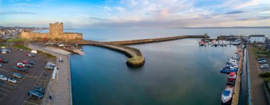 Carrickfergus, Belfast yakınlarında, Kuzey İrlanda, İngiltere. Ortaçağ Norman Kalesi 'nin geniş hava manzarası, yat marinası, tekne rampası, dalgakıran ve kışın günbatımında Belfast Lough..  