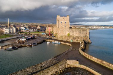 Ortaçağ Norman Kalesi, Carrickfergus 'ta tekne rampası ve dalga kırıcısı olan liman Belfast, Kuzey İrlanda, İngiltere yakınlarında. Kışın gün batımında hava manzarası. Kasaba ve fırtınalı bulutlar arka planda