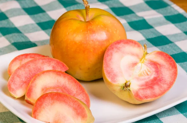 Розовые жемчужные яблоки, нарезанные на белой тарелке — стоковое фото