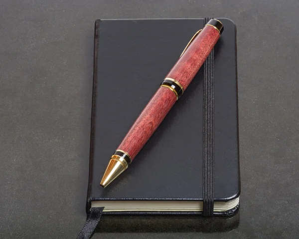 Caderno e caneta em uma mesa preta — Fotografia de Stock