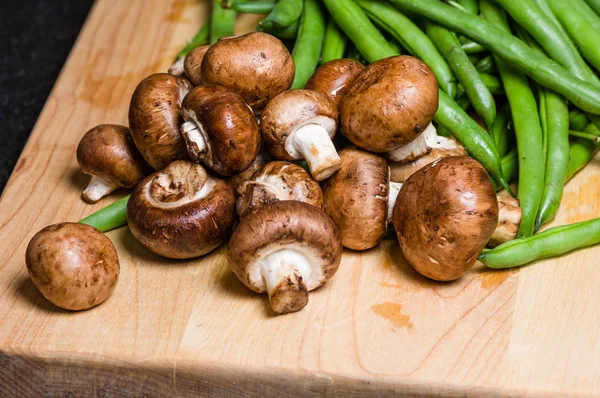 Mushrooms and green beans on a wooden board — Stock Photo, Image