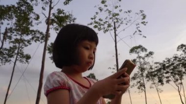 Çinli çocuk parkta ağaçlarla el telefonu oynuyor.