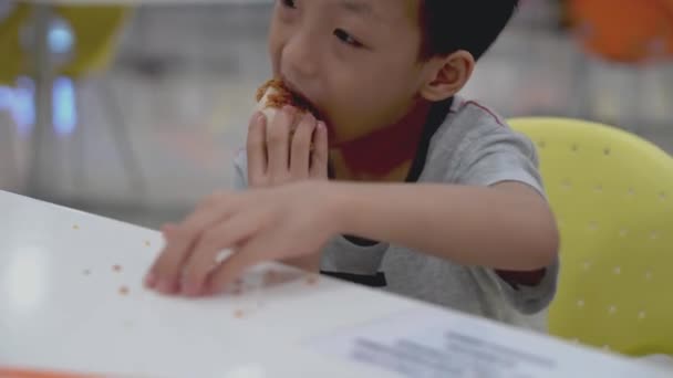 小さな子供は食べるためにテーブルの上にクリスピーな肌を収集するまでおいしいフライドチキンを食べる — ストック動画
