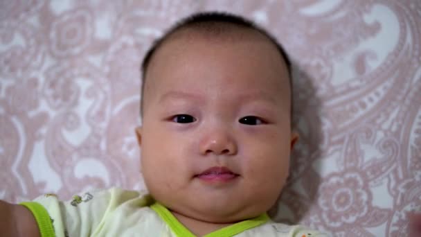 トップダウンビューアジアの赤ちゃんはベッドで横になり カメラと笑顔を見上げます — ストック動画