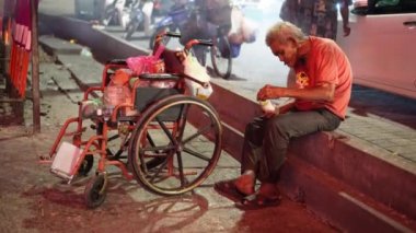 Georgetown, Penang, Malezya - 31 Ocak 2022: Tekerlekli sandalyesi olan yalnız bir adam gece yerde oturuyor