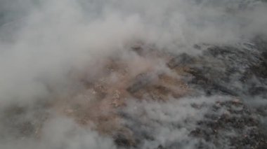 Aerial view burning and smoke at landfill site in dusk hour. An excavator and fire brigade can seen