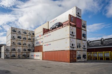 Stack of red and white containers with black car on open container on top of container stack in Sisimiut, Greenland on 16 July 2022