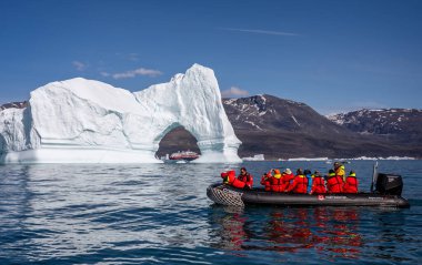 Hurtigruten's MS Fridtjof Nansen expedition  cruise ship seen through an arch in a gigantic iceberg with zodiac of intrepid tourists in foreground at Disko Bay, Greenland on 18 July 2022