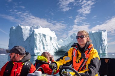 Close up of pretty young woman driving zodiac in amongst large icebergs in Disko bay, Greenland on 18 July 2022