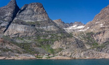 Remote settlement of  Aappilattoq dwarfed by snow capped mountains in Prince Christian Sound, South Greenland on 22 July 2022