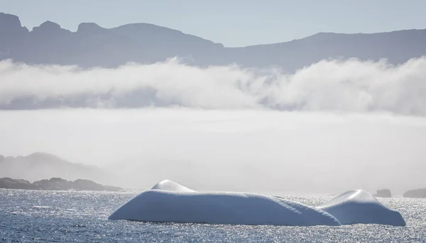 Iceberg in Prince Christian Sound with mountains and low hanging cloud in background in South Greenland