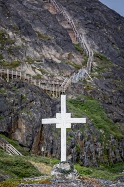 Close up of wooden cross in graveyard in front of wooden stairway up the mountain side in Maniitsoq, Greenland on 15 July 2022