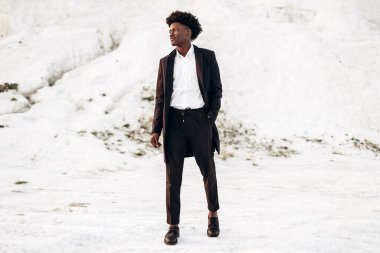 Siyah klasik takım elbiseli, modaya uygun siyah tenli Afro-Amerikalı adam, tebeşir dağlarının arka planında yürür ve poz verir, moda, erkek kıyafeti, poz verir
