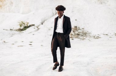 Siyah klasik takım elbiseli, modaya uygun siyah tenli Afro-Amerikalı adam, tebeşir dağlarının arka planında yürür ve poz verir, moda, erkek kıyafeti, poz verir