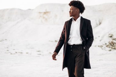 Siyah pantolonlu şık Afrikalı Amerikalı, siyah klasik ceketli, takım elbiseli siyah adam, kayalık dağların arka planında, moda pozu konsepti, erkek modası, klasik giyim tarzı