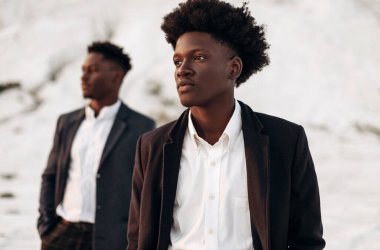 Sokakta poz veren iki manken, klasik kıyafetler, takım elbise, ceket, moda Afrikalı erkek modeller, kayaların arka planında.