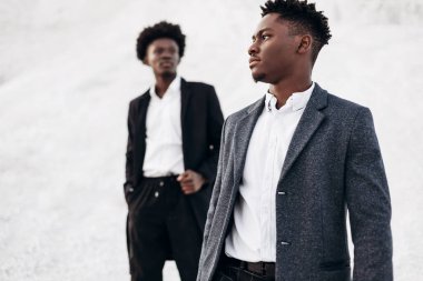 Sokakta poz veren iki manken, klasik kıyafetler, takım elbise, ceket, moda Afrikalı erkek modeller, kayaların arka planında.