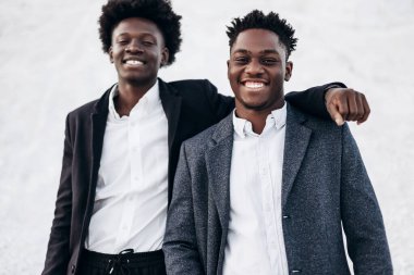 Sokakta poz veren iki mutlu siyahi adam, klasik siyah takım elbiseli arkadaşlar, moda, erkek giyim, alışveriş,