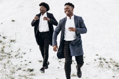 Havalı Afro-Amerikan kıvırcık saçlı, şık, benzer takım elbiseli adamlar, gün batımında kayalık bir bölgede moda pozu veriyorlar.