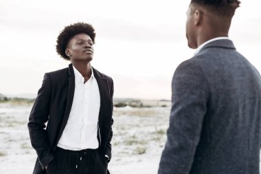 Sokakta poz veren iki mutlu siyahi adam, klasik siyah takım elbiseli arkadaşlar, moda, erkek giyim, alışveriş,