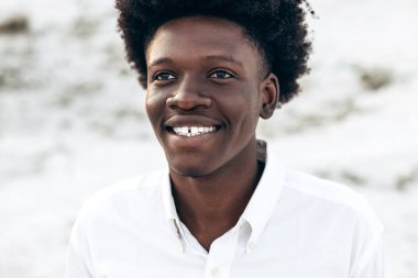 Beyaz dişli mükemmel bir gülümseme ile, şık kıvırcık saçlı siyah bir adam portresi, bir manzara arka plan karşı kamera bakıyor