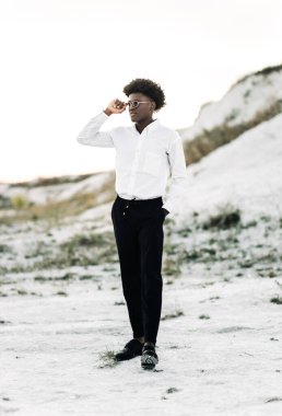 Yakışıklı Afro-Amerikan hippi, şık güneş gözlüklü ve beyaz gömlekli, sokakta poz veren, moda, moda, tarz