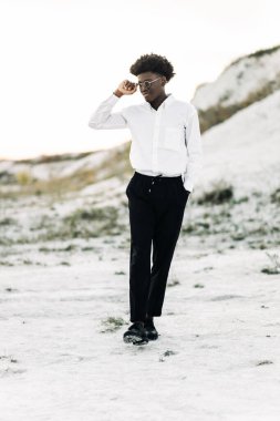 Yakışıklı Afro-Amerikan hippi, şık güneş gözlüklü ve beyaz gömlekli, sokakta poz veren, moda, moda, tarz