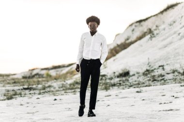 Yakışıklı Afro-Amerikan hippi, şık güneş gözlüklü ve beyaz gömlekli, sokakta poz veren, moda, moda, tarz