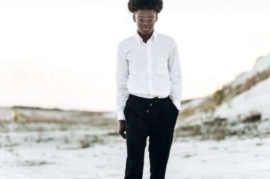 Yakışıklı Afro-Amerikan hippi, şık güneş gözlüklü ve beyaz gömlekli, sokakta poz veren, moda, moda, tarz