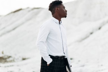 Beyaz klasik gömlekli, yakışıklı, şık bir Afrikalı Amerikalı adamın portresi. Elinde dizüstü bilgisayar, arka planda güzel bir manzara ve dağlarda.