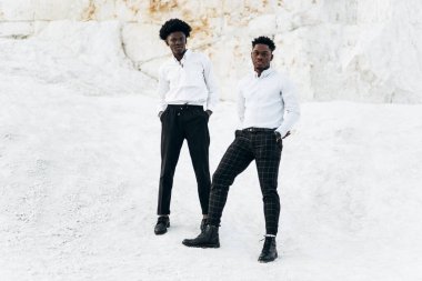 İki zarif siyah Afrikalı, beyaz gömlekli, tam gelişim içinde, dağların ve kayaların yanında açık havada poz veriyorlar, arkasında güzel bir manzara olan moda, moda pozu veriyorlar.,