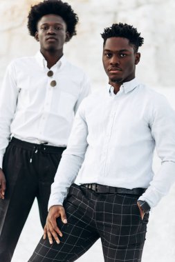 İki modaya uygun siyah adam, beyaz gömlekli Afro-Amerikan erkek modellerin moda portresi, açık havada tebeşir dağları ve kayaların arka planına karşı