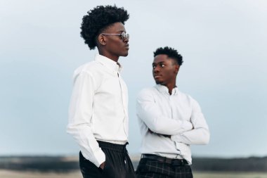 İki kendinden emin Afrikalı Amerikalı, dağın zirvesinde duruyor, kayalara tırmanıyor, iş adamı başarısı, gün batımında dağın zirvesinde yürüyüş yapıyor, kazanan lider konsepti.