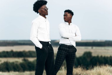 İki kendinden emin Afrikalı Amerikalı, dağın zirvesinde duruyor, kayalara tırmanıyor, iş adamı başarısı, gün batımında dağın zirvesinde yürüyüş yapıyor, kazanan lider konsepti.