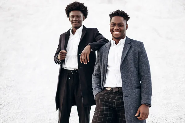 Sokakta poz veren iki manken, klasik kıyafetler, takım elbise, ceket, moda Afrikalı erkek modeller, kayaların arka planında.